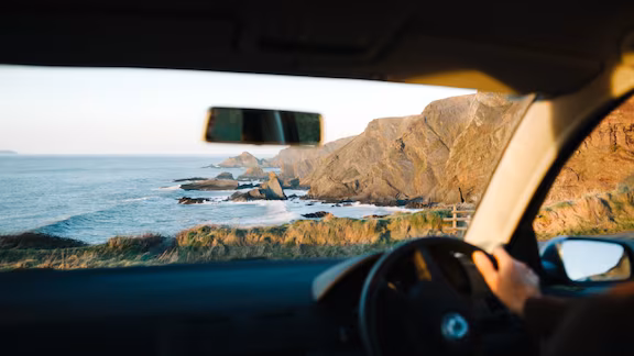 A driver looks out at mountains lining the ocean shore