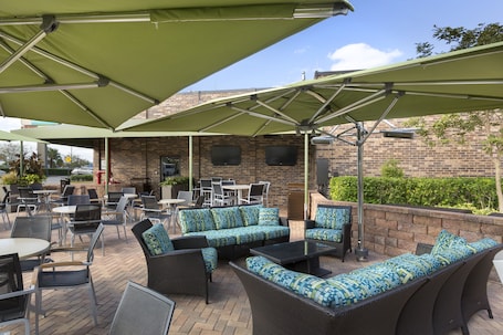 An outdoor patio with wicker furniture, green umbrellas, and brick walls.