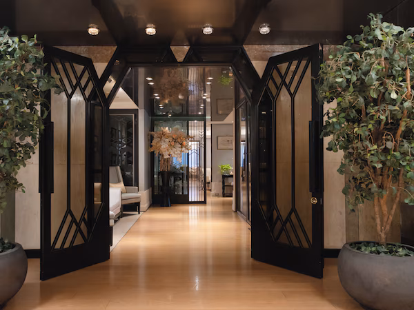 A hallway with a modern design, featuring a geometric black gate, potted plants, and a light-colored floor.