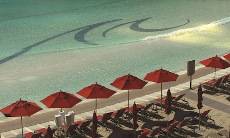 A beachside area with rows of red umbrellas and lounge chairs facing the ocean.