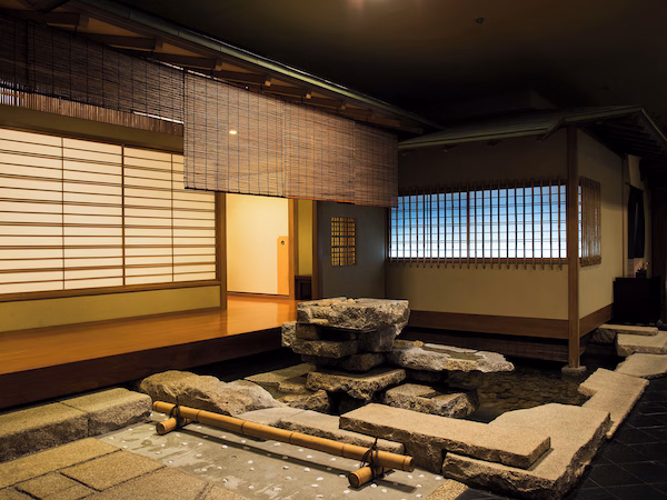 A traditional Japanese interior with tatami flooring, sliding doors, and a stone water feature.