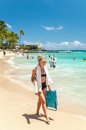 A beach scene with clear turquoise water, people swimming and walking along the shore, and palm trees in the background.