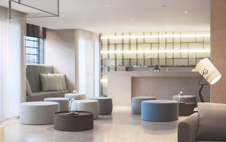 A modern living room with a sofa, ottomans, and a lamp.