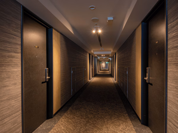 A long, narrow hallway with wooden walls and doors, leading to a bright end.