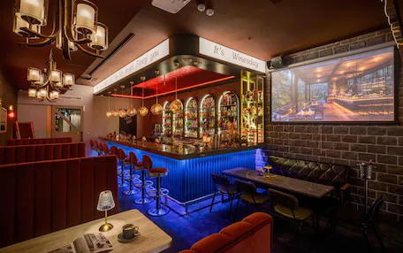 A bar area with a red-lit bar counter, multiple hanging lights, and a projection screen displaying a scenic view.
