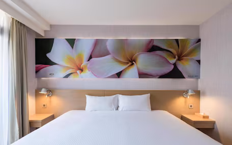 A hotel room with a large bed, two bedside tables, and a wall-mounted artwork of flowers.