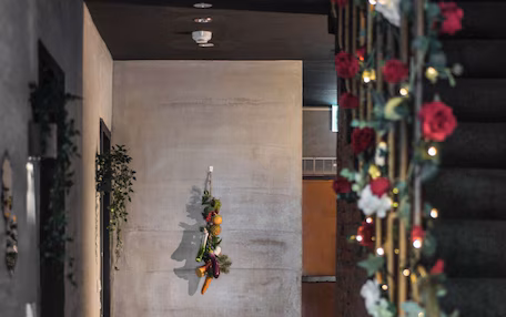 A hallway with a concrete wall, a hanging fruit decoration, and a staircase with red flowers and lights.