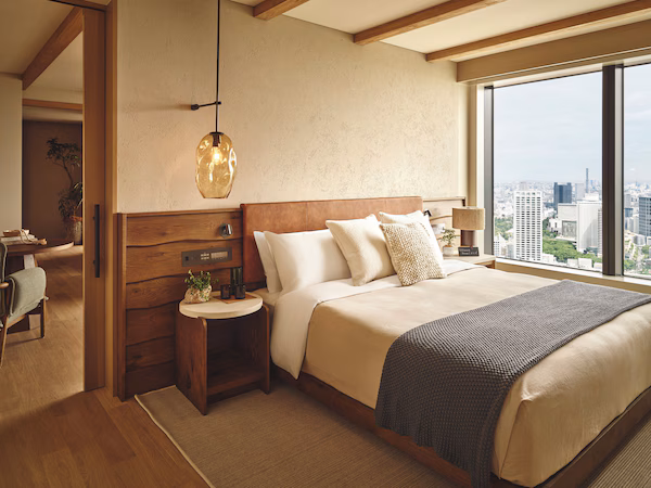 A modern bedroom with a large bed, bedside tables, a desk, and a view of the city.