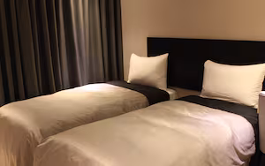 A hotel room with two beds, dark curtains, and a black headboard.