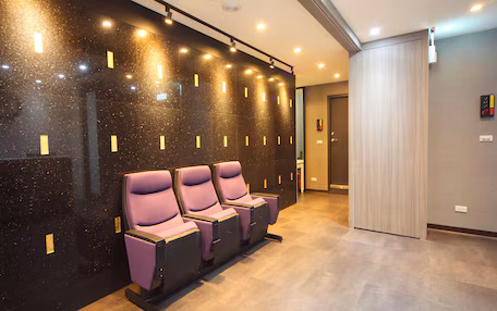 A modern waiting area with a black marble wall and recessed lighting. There are three purple chairs aligned in a row.