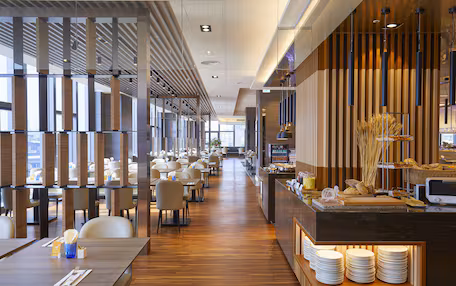 A modern restaurant with wooden paneling, a long counter with plates, and multiple tables with chairs.