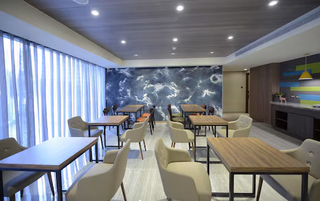 A modern restaurant with wooden tables and chairs, a large mural on the back wall, and a bright ceiling with recessed lighting.