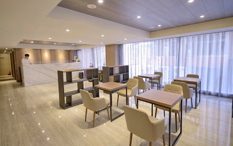 A modern hotel lobby with a reception desk, seating area, and large windows.