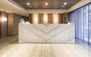 A reception area with a marble reception desk, wooden panel walls, and a large window with curtains.