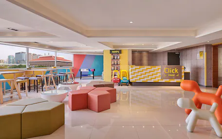 A modern hotel lobby with a 'Click Hotel' reception, seating areas, and a view of the cityscape.