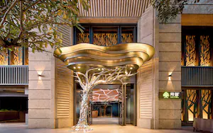 A modern hotel entrance with a unique tree-shaped light installation and a visible sign for the hotel.