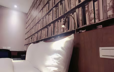 A bedroom with a large bed, a wooden headboard, a bookshelf filled with books, and a desk with a chair.