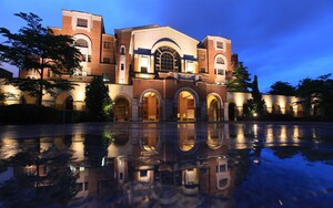 A large, historic building with arched windows and a central dome, reflecting in a pool in front.