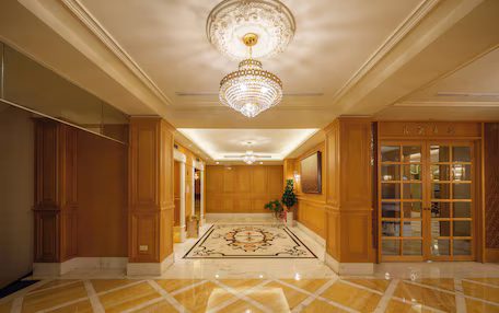 A spacious lobby with a marble floor, wooden paneling, a chandelier, and a glass door entrance.