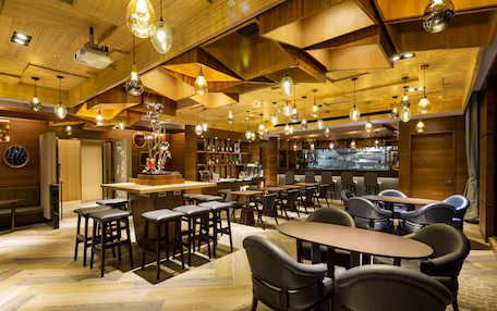 A modern bar area with wooden ceiling, multiple hanging light fixtures, and bar stools.