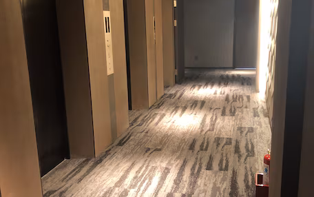 A hotel hallway with carpeted floors, multiple doors, and ceiling lights.