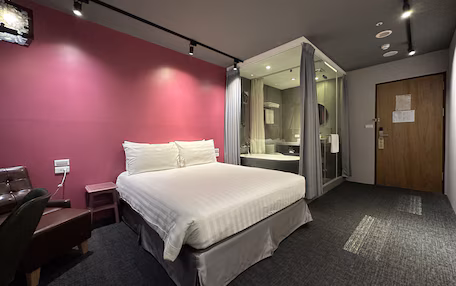 A hotel room with a bed, a desk, a chair, a shower area, and a door.