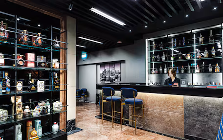 A bar area with shelves of liquor bottles, a marble counter, and bar stools.