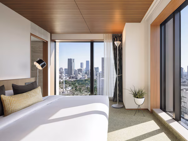 A modern hotel room with a large bed, city view, and a potted plant.