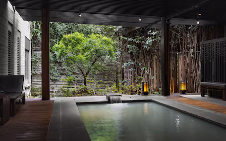 A serene indoor pool area with a wooden deck, seating, and a waterfall feature.