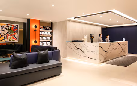 A modern reception area with a marble reception desk, a sofa with black cushions, and a colorful abstract painting on the wall.