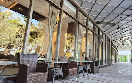 An outdoor seating area with wicker chairs and tables, large windows, and a covered walkway.