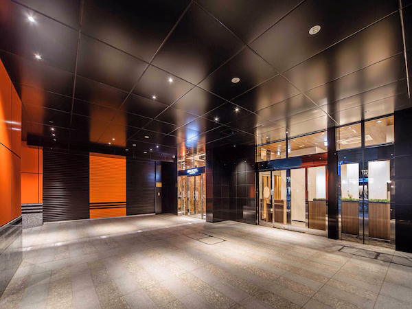 A modern hotel lobby with a spacious open area, glass doors leading to the reception, and a prominent hotel sign.