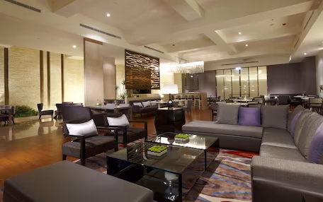 A spacious lobby with a modern design, featuring a mix of seating areas, a reception desk, and a decorative wall.