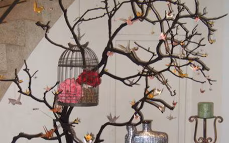 A table with a red tablecloth, a decorative tree with branches, a birdcage, and a vase with flowers.