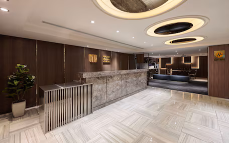 A modern hotel lobby with a reception desk, seating area, and a large potted plant.