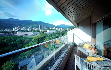 A balcony with a glass railing overlooking a cityscape with mountains in the background.
