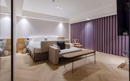 A modern hotel room with a bed, sofa, and a small table.