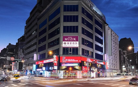 A multi-story hotel with a prominent 'MUZIK' sign, featuring a modern architectural design with a glass facade and multiple balconies.
