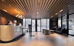 A modern reception area with a curved reception desk, seating area with sofas, large windows, and a wooden ceiling.