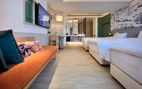 A hotel room with a sofa, two beds, a desk, and a large mirror.
