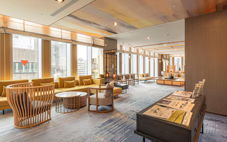 A spacious lobby with a modern design, featuring a mix of seating areas, a coffee bar, and a reception desk.