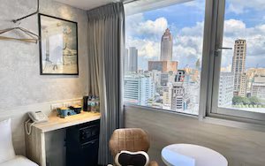 A hotel room with a city view, a desk with a phone, a chair, and a small table.